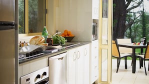 A modern kitchen with white cabinets, a black countertop, and a window overlooking a garden. - Falls Mountain Retreat (Wentworth Falls)