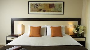 A neatly made bed with white and orange pillows, a framed artwork above, and a nightstand with a lamp and flowers. - Falls Mountain Retreat (Wentworth Falls)