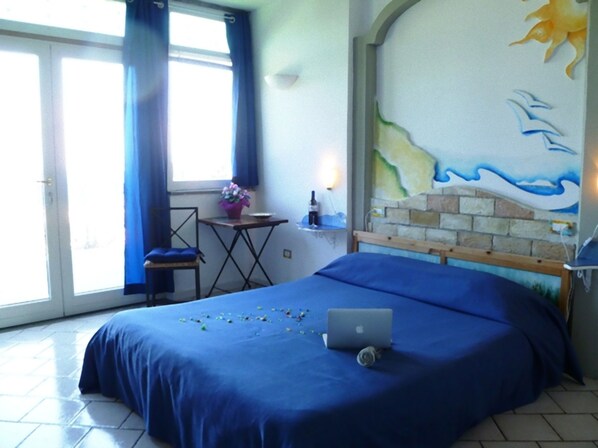 A bedroom with a bed, a laptop, a small table with a bottle, and a chair.