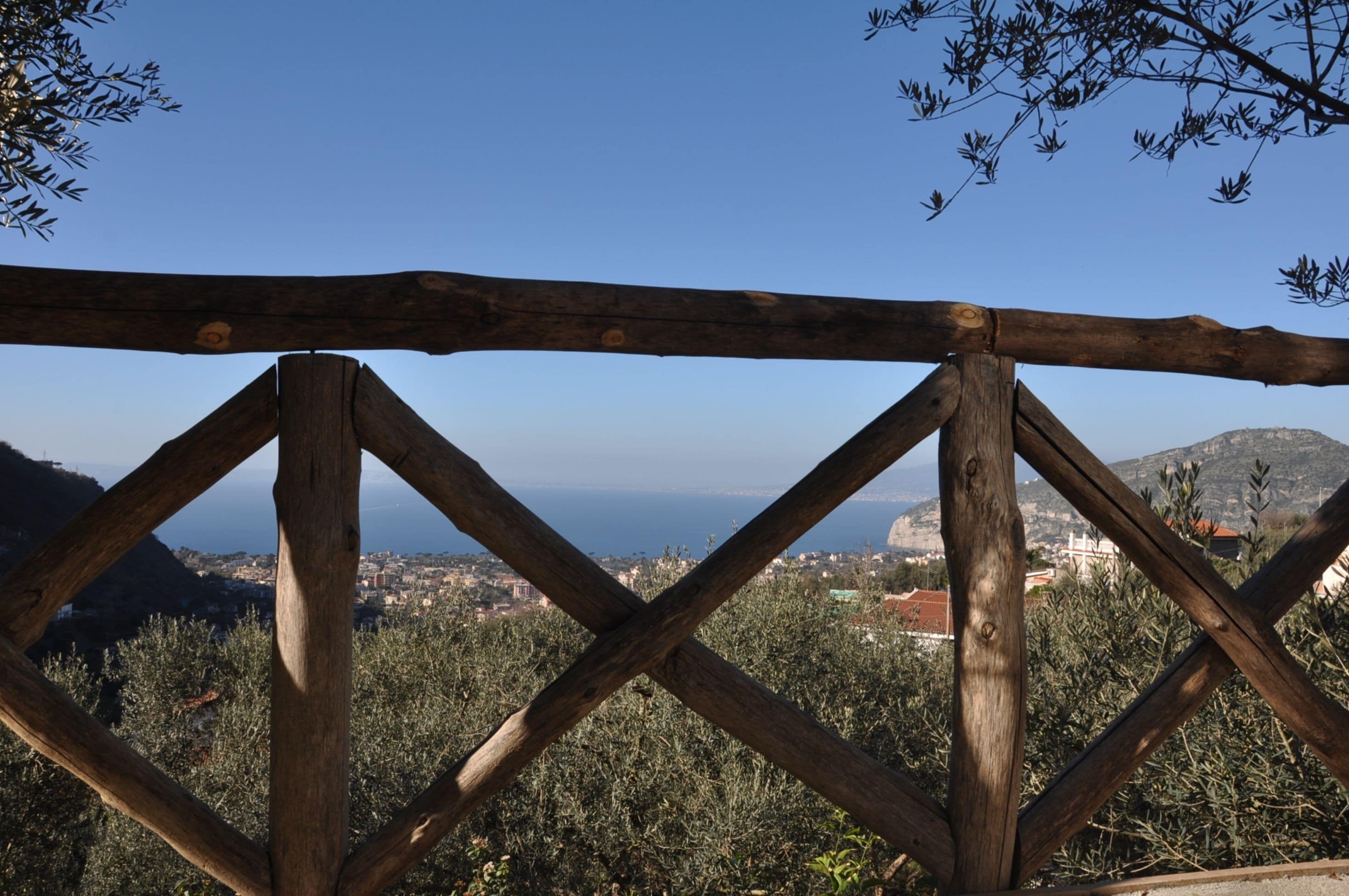 A wooden fence with a view of a coastal town and mountains in the background.