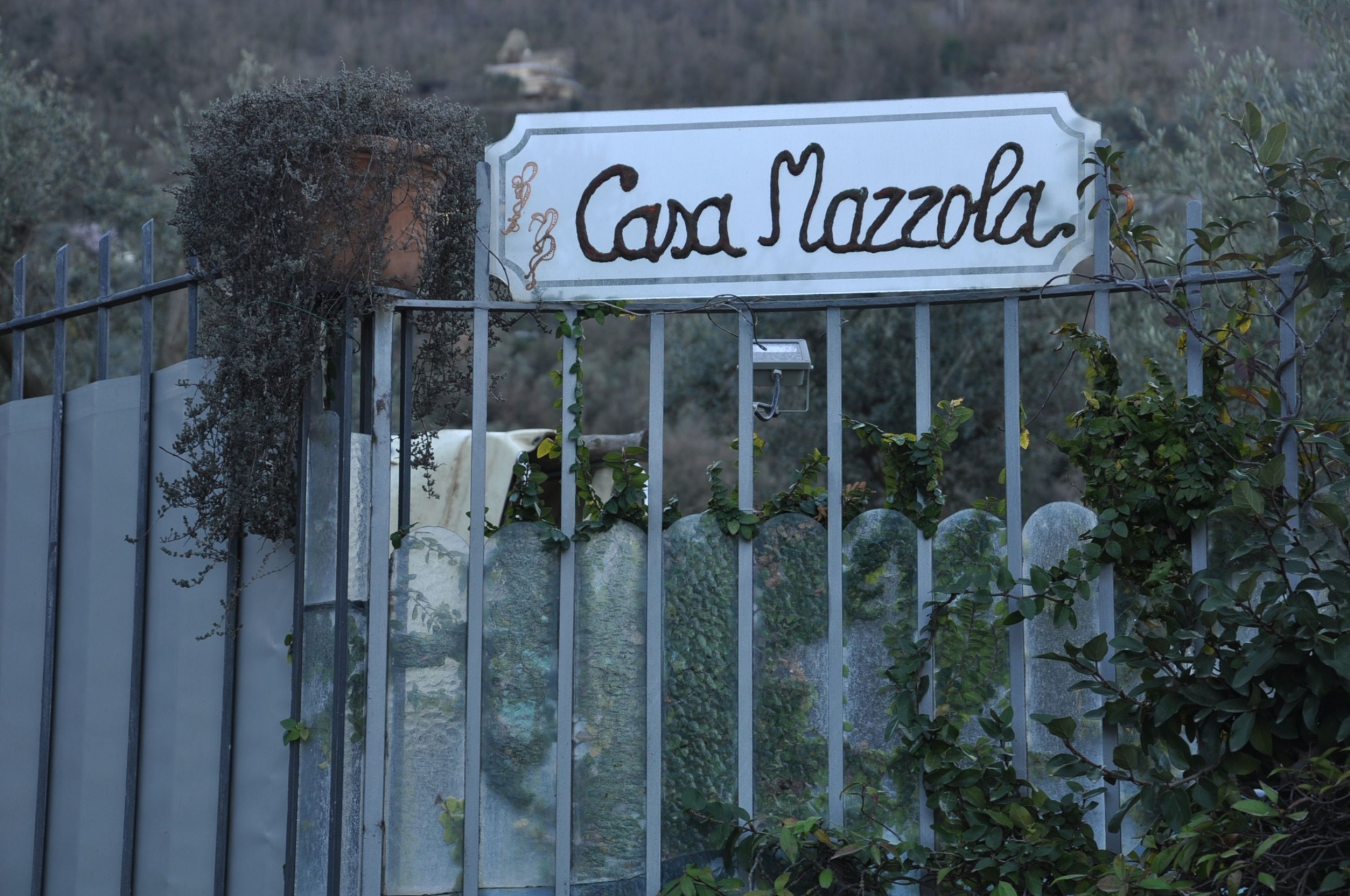 Une enseigne indiquant « Casa Mazzola » est fixée à une clôture en métal, le tout agrémenté de verdure.