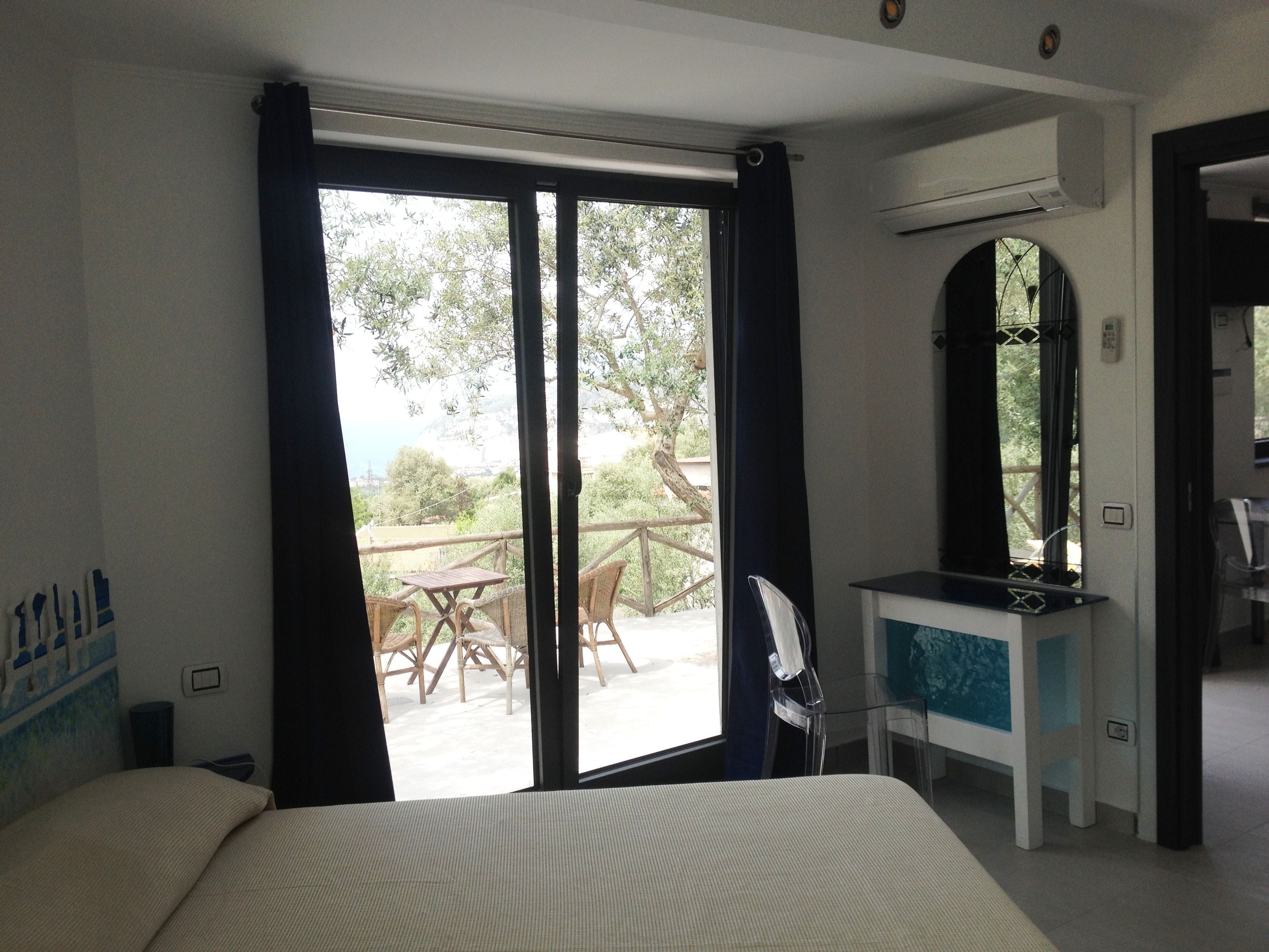 A hotel room with a bed, a desk, a chair, and a view of the outdoors through a sliding door.