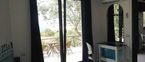 A hotel room with a bed, a desk, a chair, and a view of the outdoors through a sliding door.
