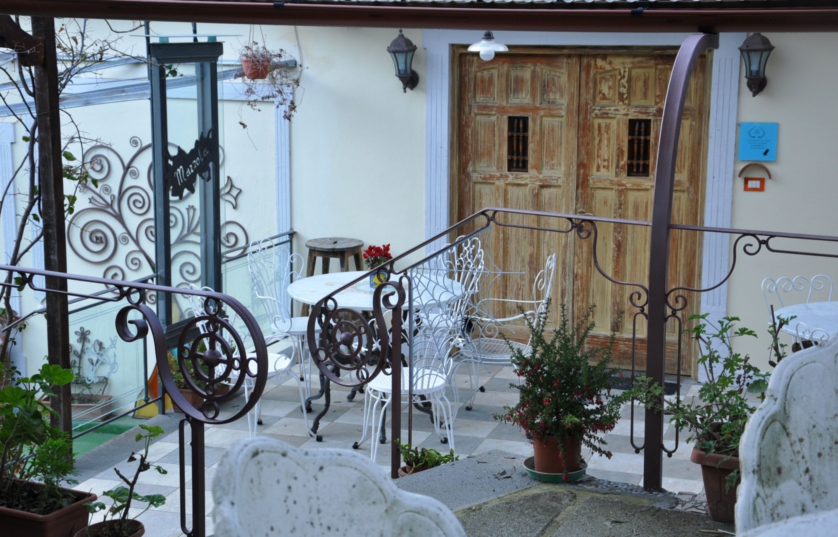 Une cour avec une porte en bois, des chaises en métal, une petite table et des plantes en pot.