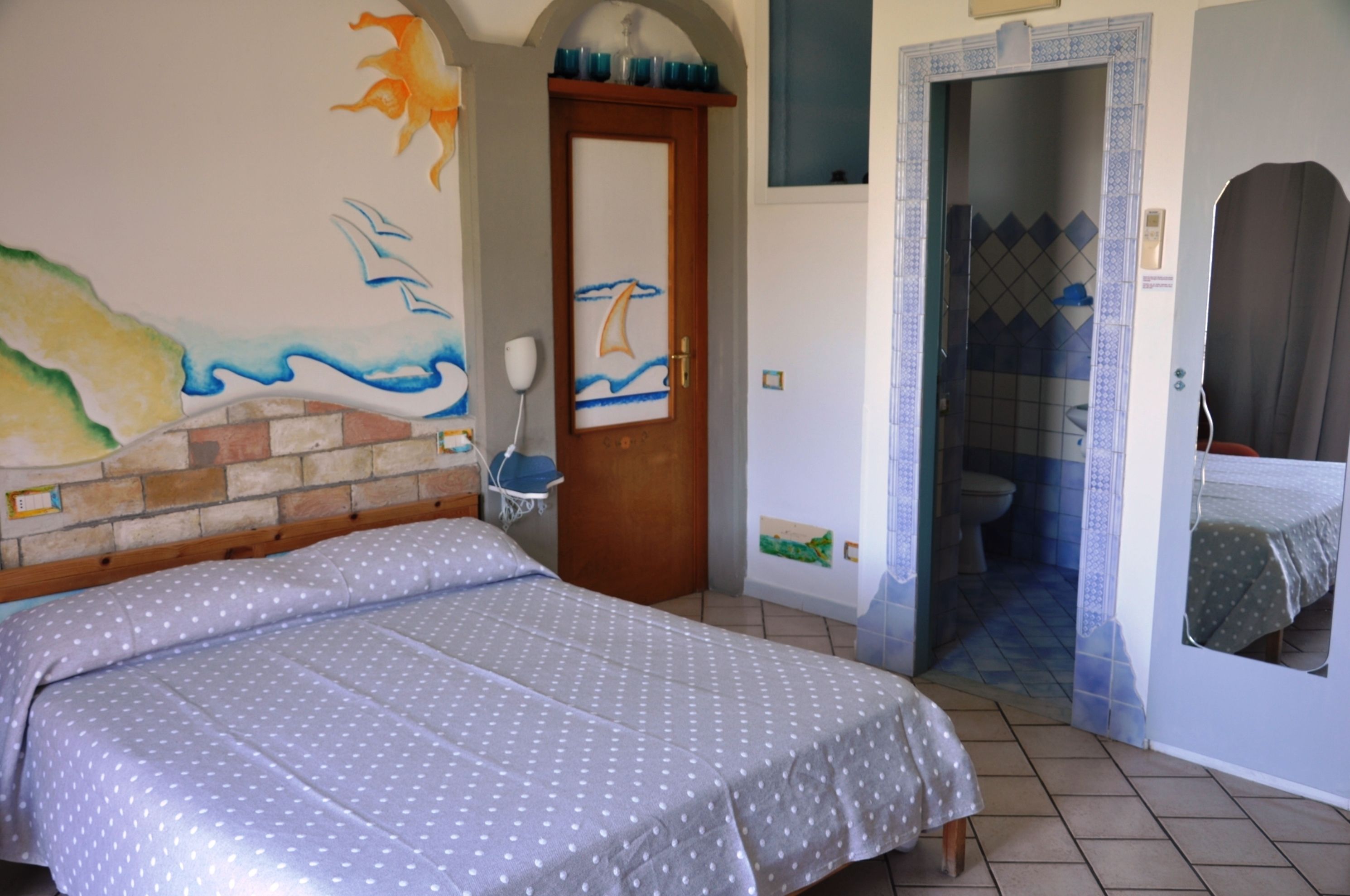 A bedroom with a bed, a bathroom with a shower, and a door with a nautical mural.