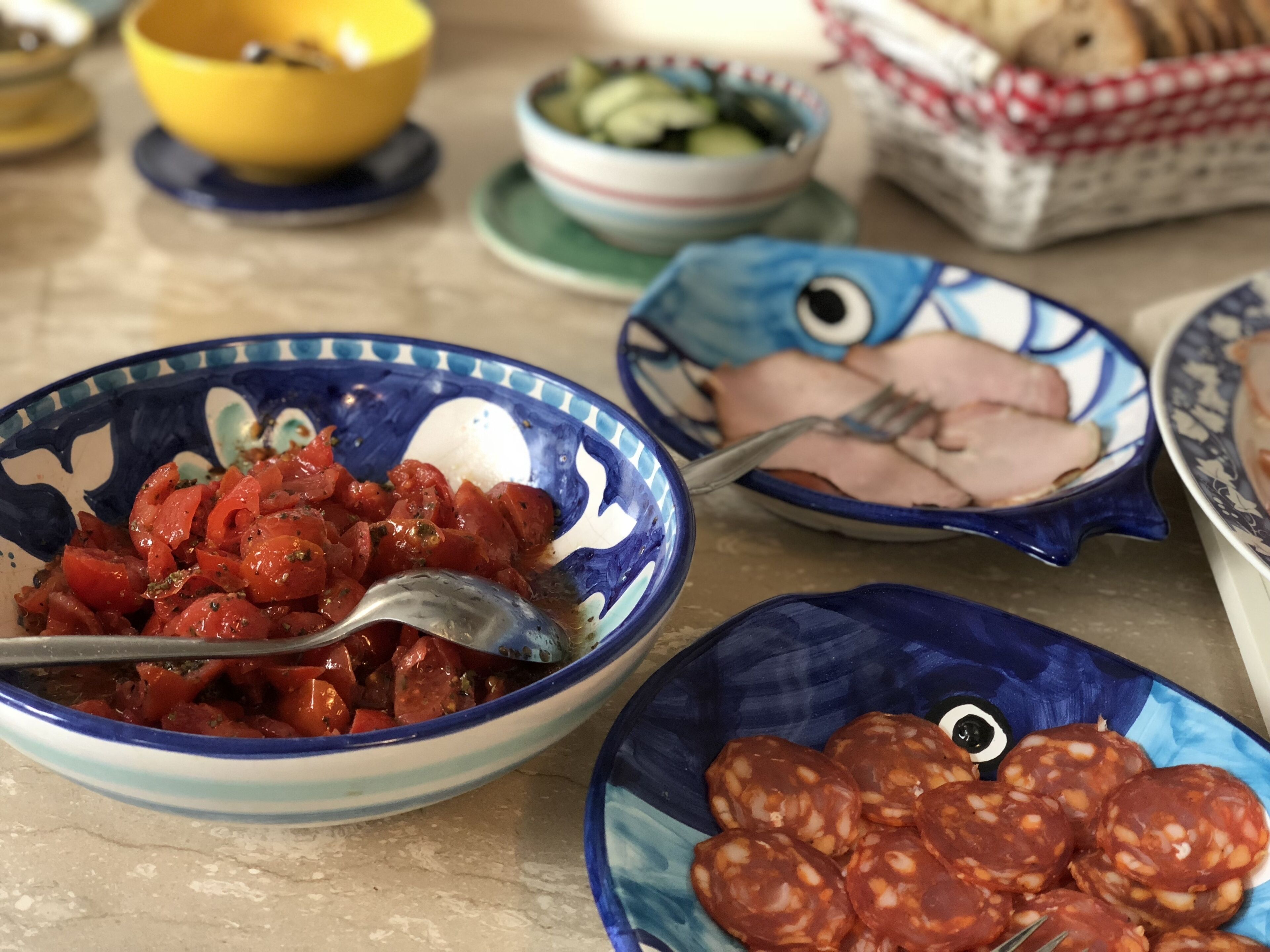 A table with various dishes including a bowl of tomato salad, a plate of sliced ham, and a plate of salami.
