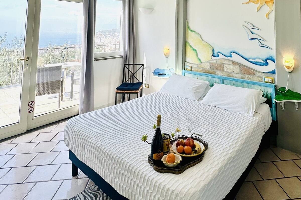 A bedroom with a bed, a view of the city, a balcony, and a mural on the wall.