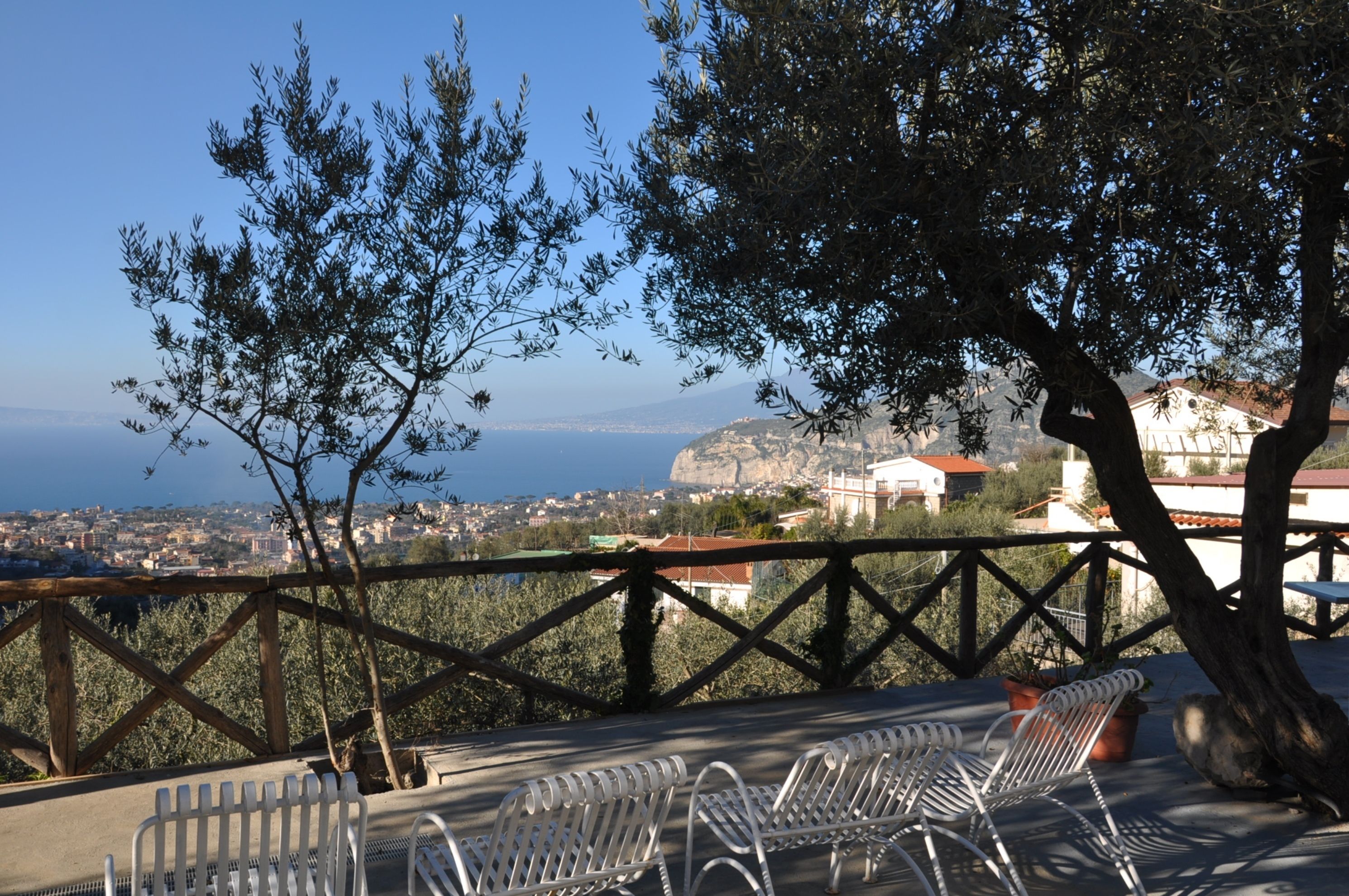 A terrace with metal chairs and a view of a coastal town.