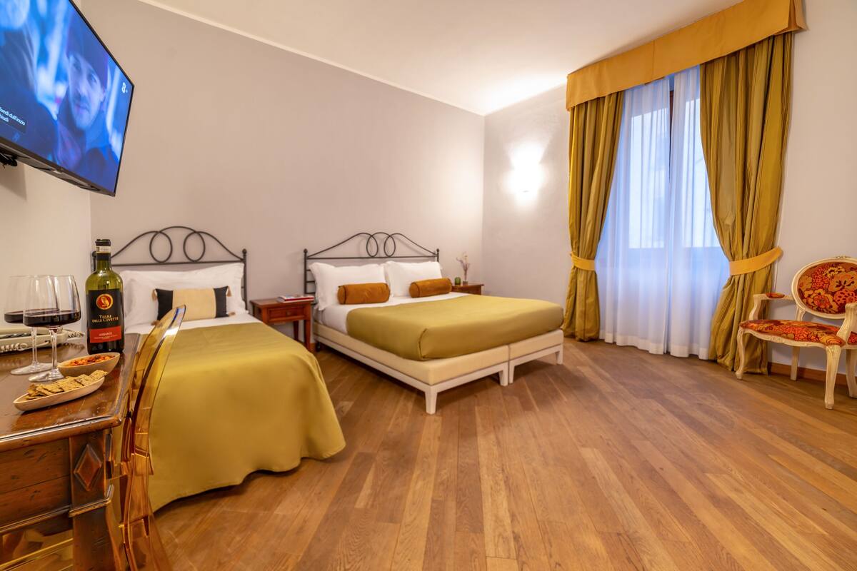 A hotel room with two beds, a TV, a dining table with a chair, and a window with curtains.