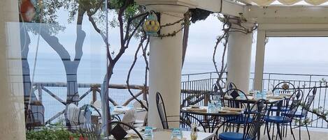 An outdoor seating area with tables and chairs, surrounded by a decorative border, and featuring a view of the sea.
