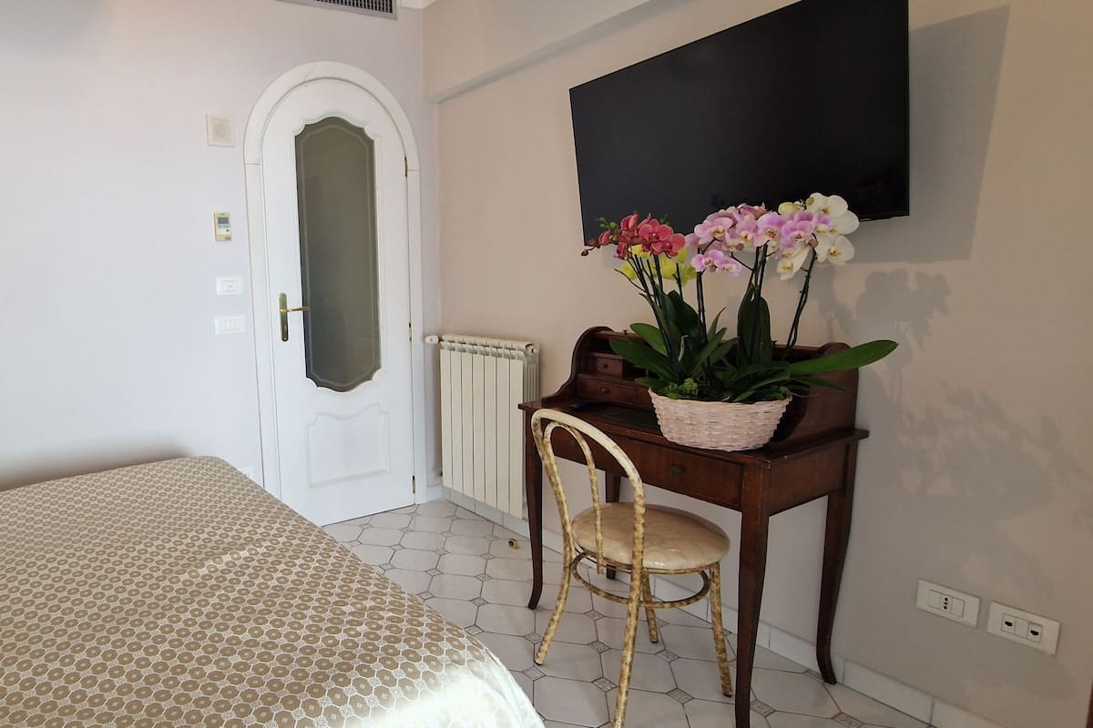 A bedroom with a bed, a desk with a chair, a radiator, and a TV mounted on the wall.