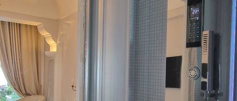 Habitación de hotel con una cama grande, un baño con panel de control digital para la ducha y vista hacia la habitación contigua.