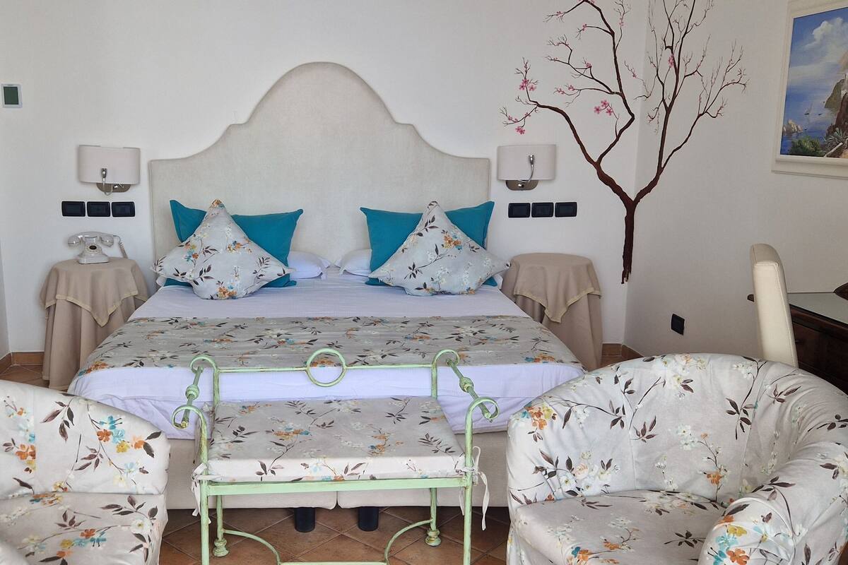 A bedroom with a bed, two nightstands, a chair, a small table, and a painting on the wall.