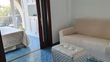 A room with a beige sofa, a patterned ottoman, and a bed with a patterned bedspread.