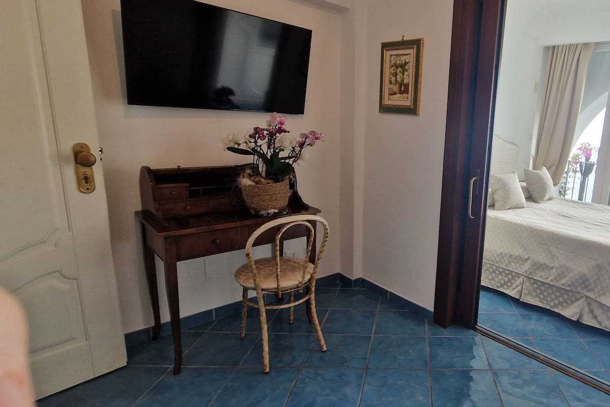 A bedroom with a bed, a desk with a chair, a television, and a balcony with a view.