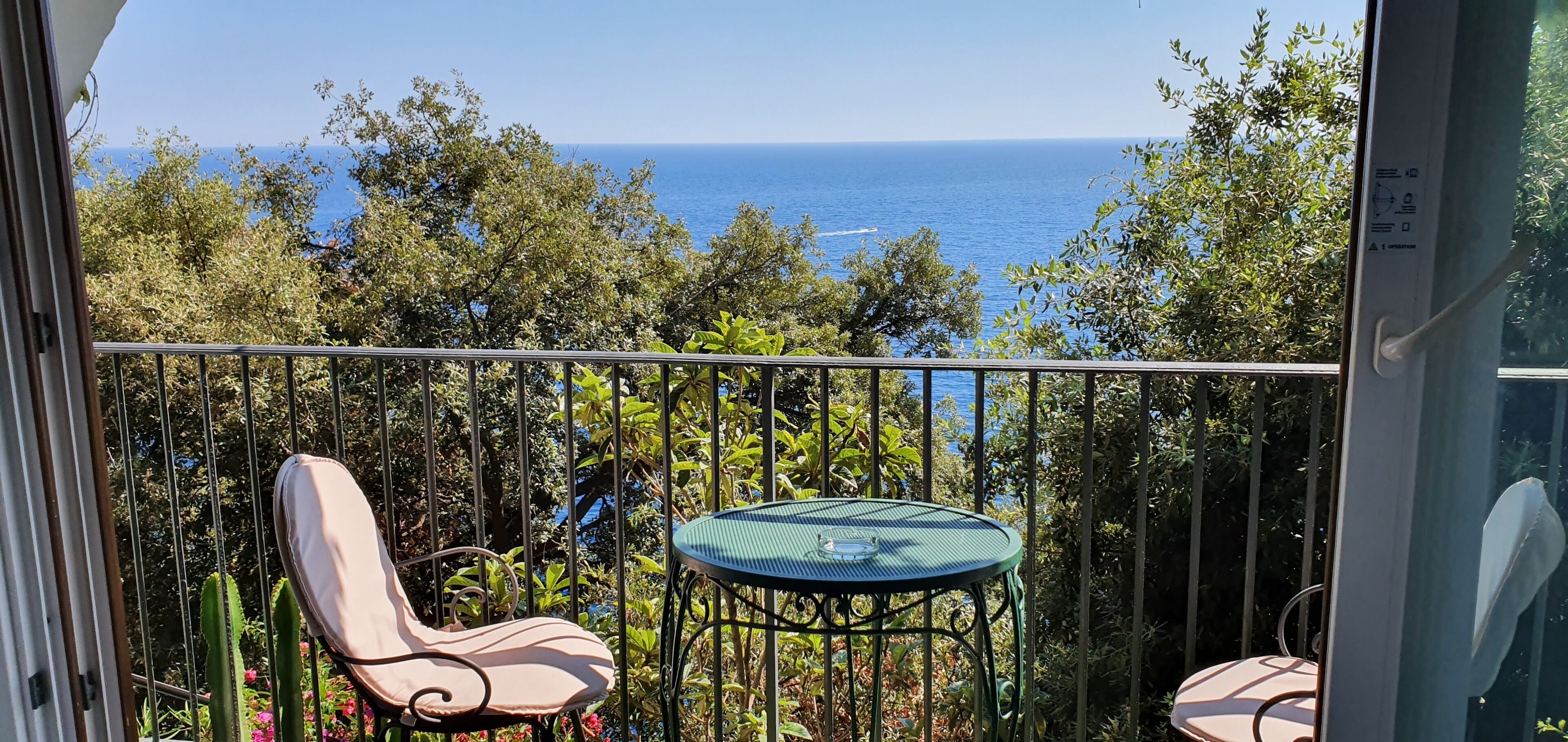A balcony with a view of the sea, a table, and two chairs.