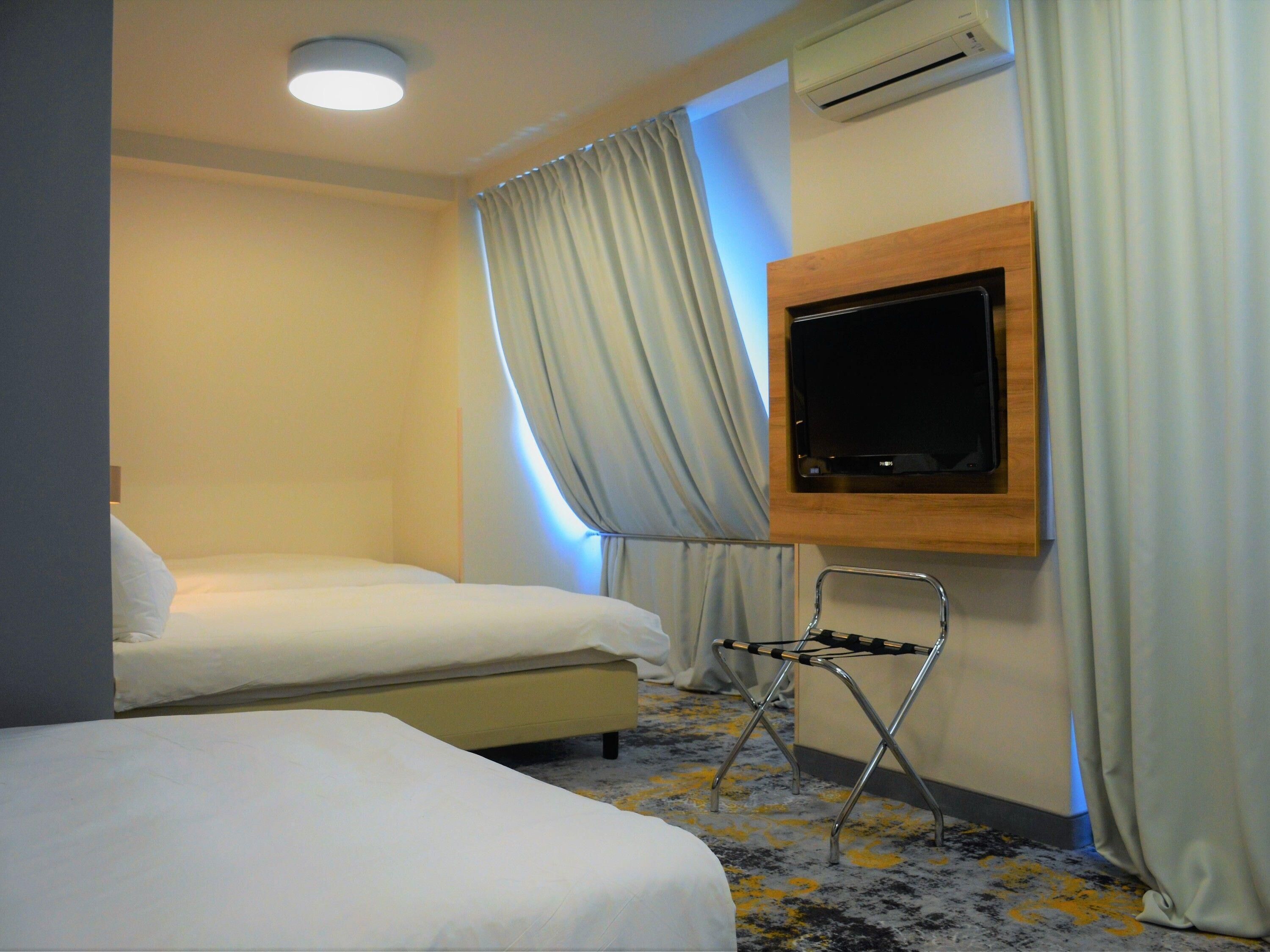 Habitación de hotel con dos camas, un televisor montado en la pared y un equipo de aire acondicionado.