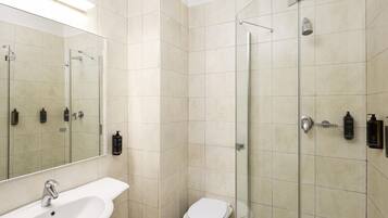 Un baño moderno con cabina de ducha de vidrio, un lavamanos blanco y un inodoro.