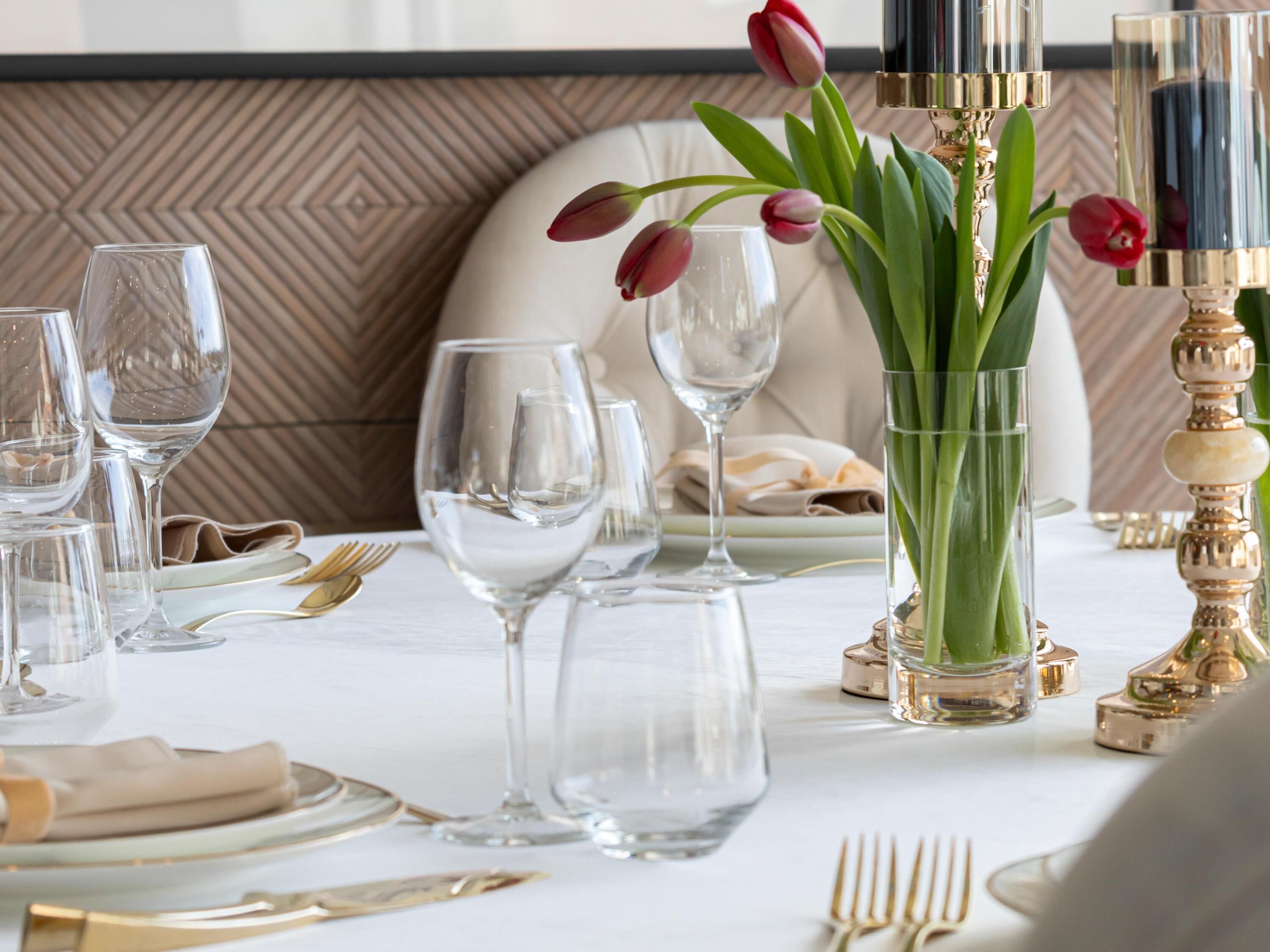Mesa dispuesta para comer, con cristalería transparente, un jarrón con tulipanes y vajilla elegante.