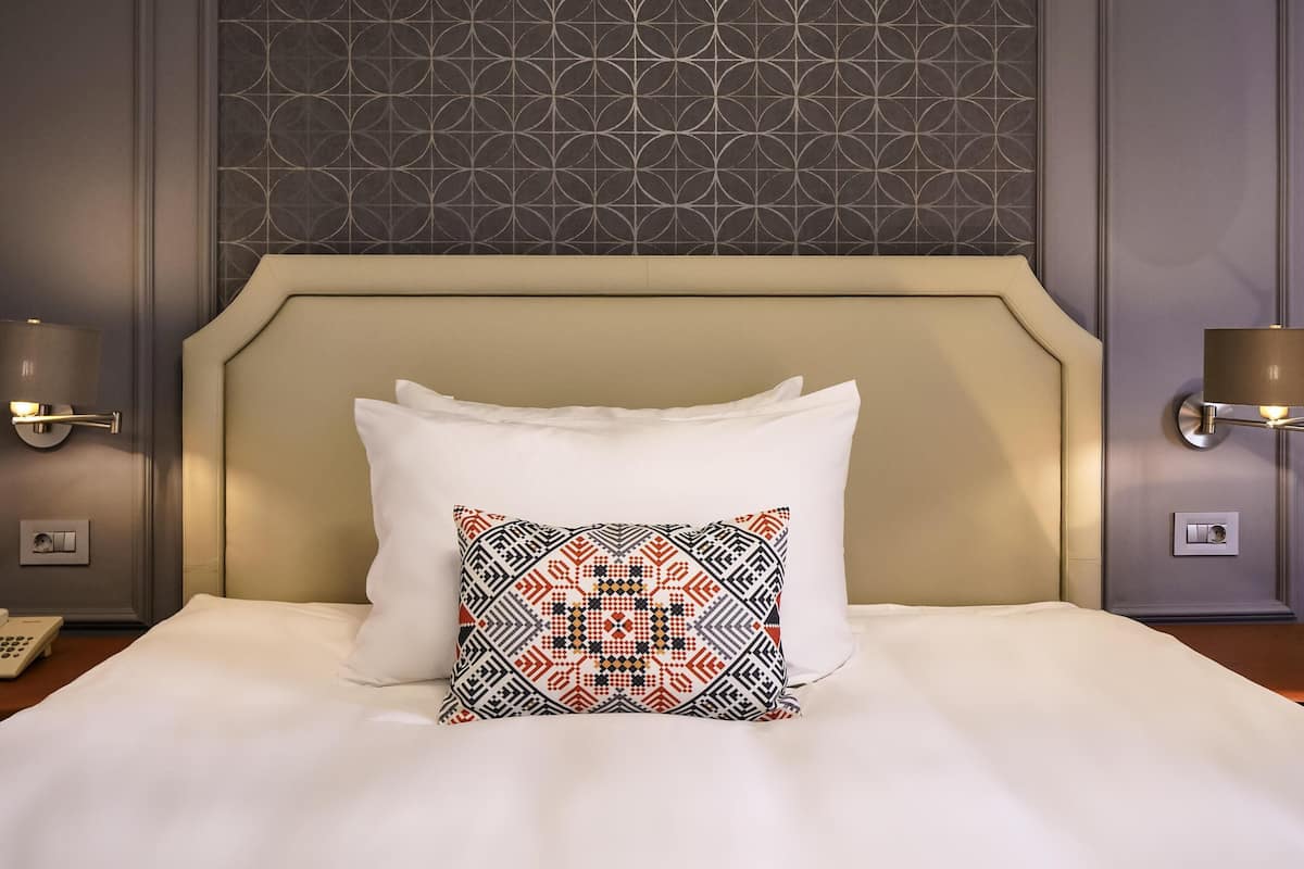 Ein Hotelzimmer mit einem großen Bett, einem gemusterten Zierkissen und Wandleuchten.