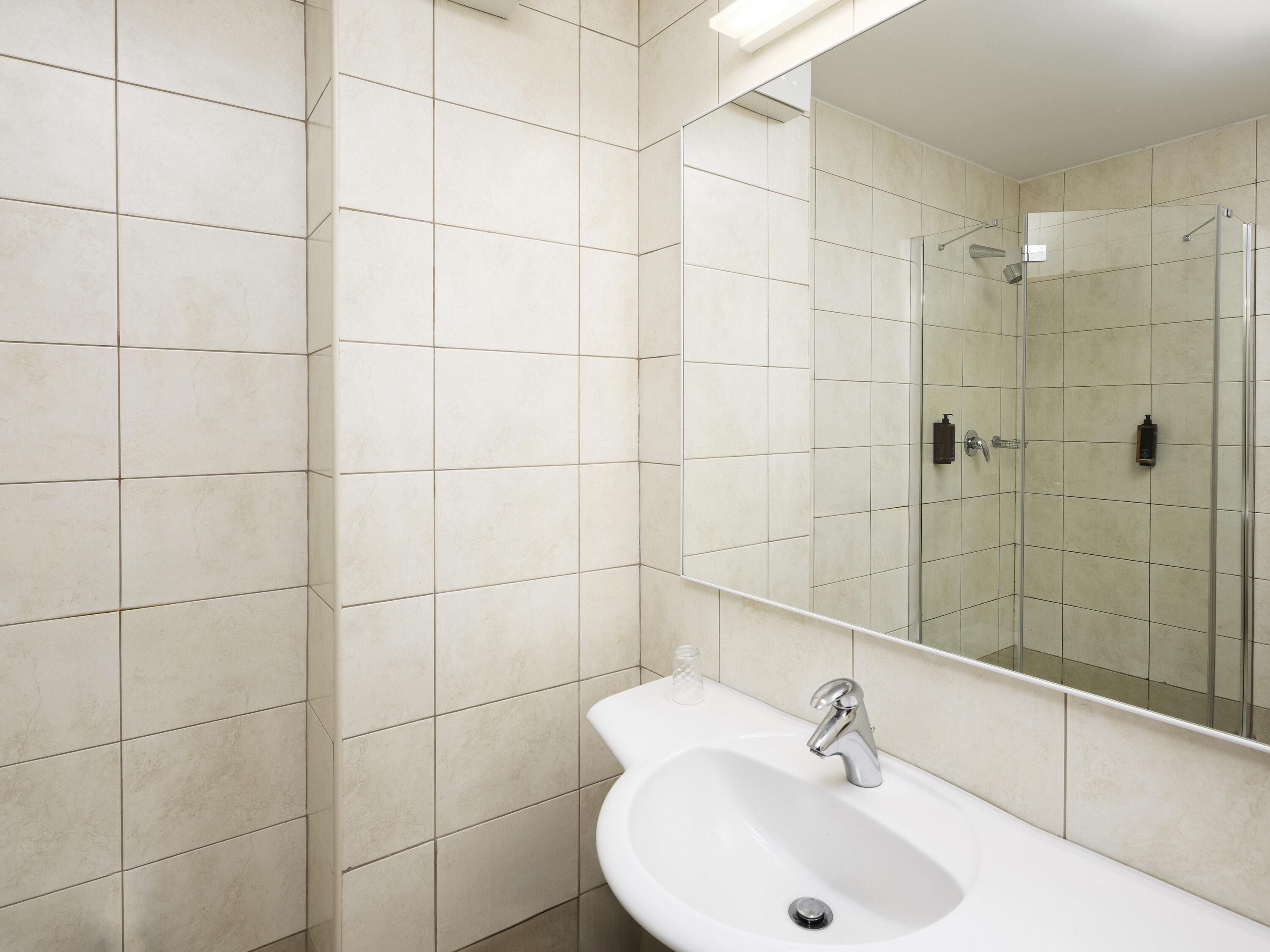 Un baño moderno con un lavabo blanco, un espejo y una cabina de ducha de vidrio.
