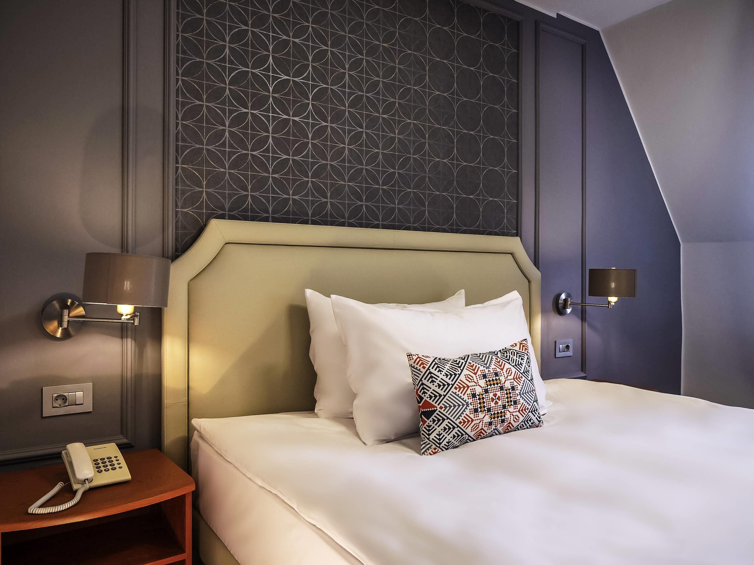A hotel room with a bed, two bedside lamps, a telephone, and a patterned pillow.
