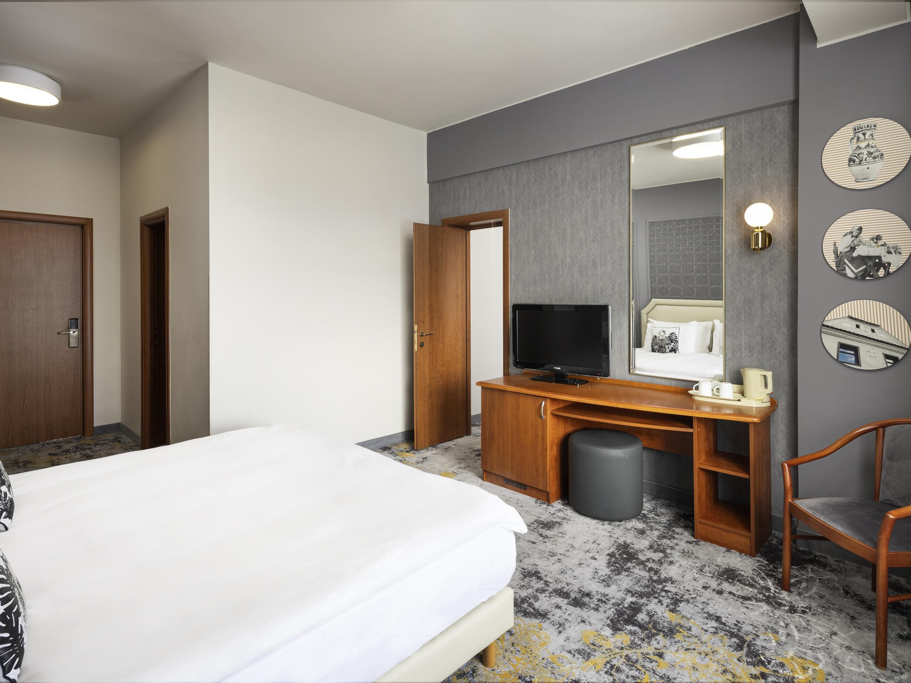 A hotel room with a bed, a desk with a television, a chair, a trash bin, and a wall with decorative plates.