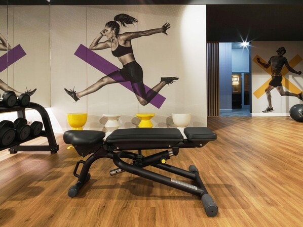Un gimnasio con equipamiento de ejercicio, una pared con un mural dinámico y suelo de madera.