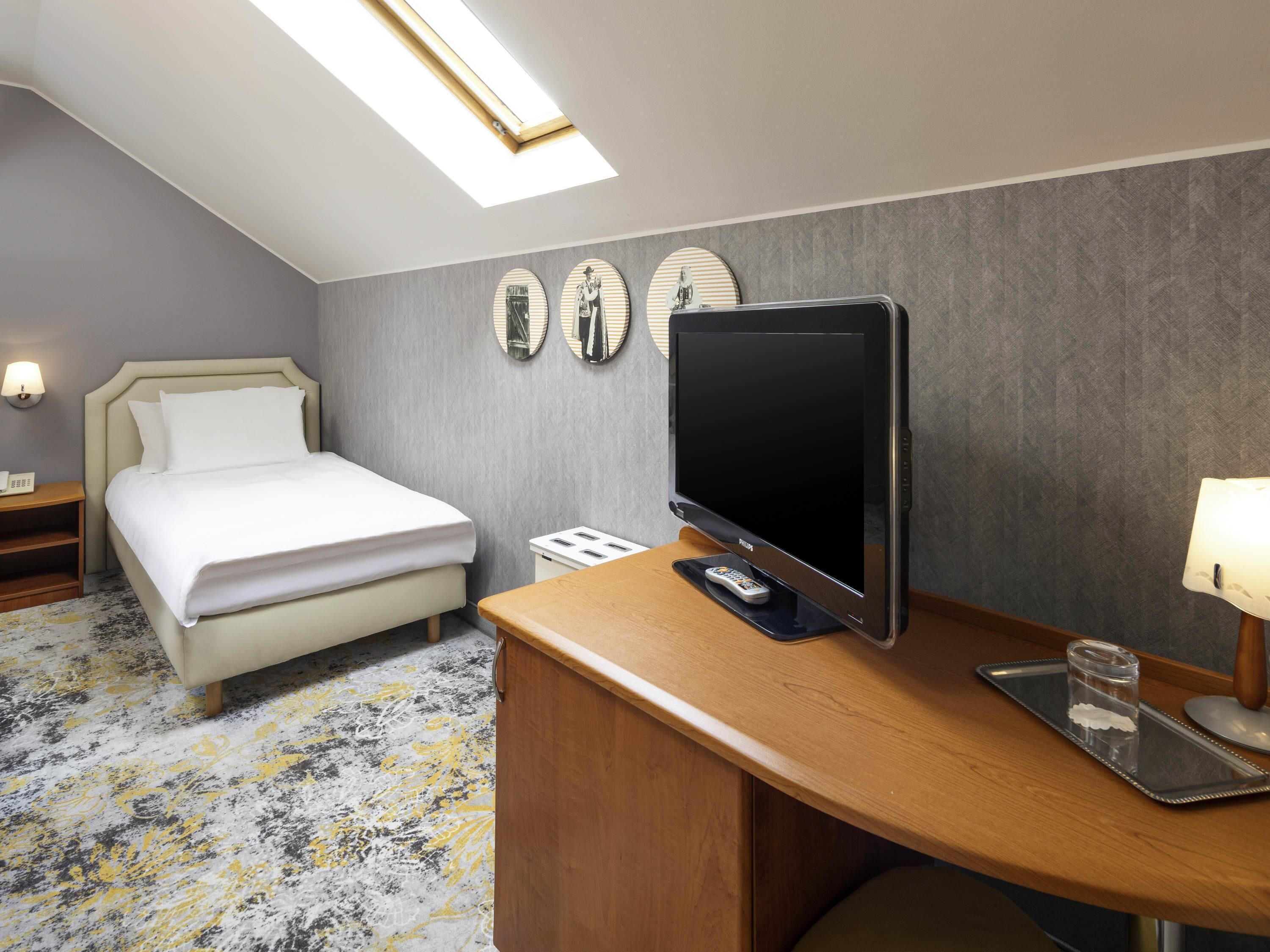 Habitació d'hotel amb un llit, una taula de nit, un escriptori amb televisió i una làmpada.