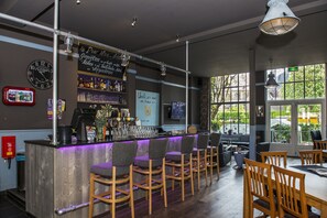 Una zona de bar con mostrador de madera, taburetes y vistas al exterior a través de amplias ventanas.