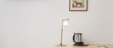 Une chambre avec un lit, un bureau doté d’une lampe, une bouilloire et un tableau encadré au mur.