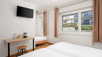 Ein Hotelzimmer mit Bett, Schreibtisch, Stuhl, Fernseher und einem Fenster mit Vorhängen.