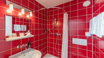 A bathroom with red tiled walls, a white sink, a bathtub, a shower with a curtain, and a mirror with lights.