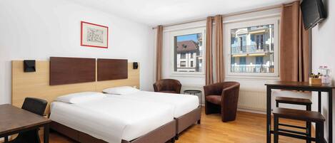 Ein Hotelzimmer mit einem großen Bett, einem Schreibtisch, zwei Stühlen, einem Fernseher und einem Fenster mit Blick auf Gebäude.