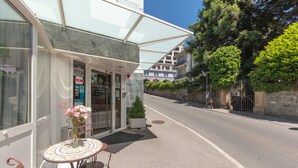 A hotel entrance with a covered outdoor seating area, a small potted plant, and a clear sky. - Hôtel Bon Port (Montreux)