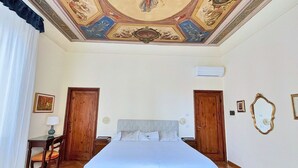 Un dormitorio con una cama grande, suelo de madera, dos puertas, un techo con un mural y un aire acondicionado instalado en la pared.