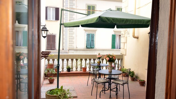 Un patio exterior con dos mesas redondas, sombrillas verdes y plantas en macetas.