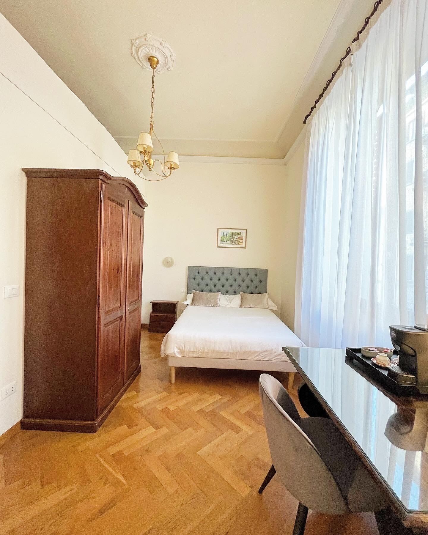 Une chambre d’hôtel avec un lit, un bureau, une armoire et un lustre.