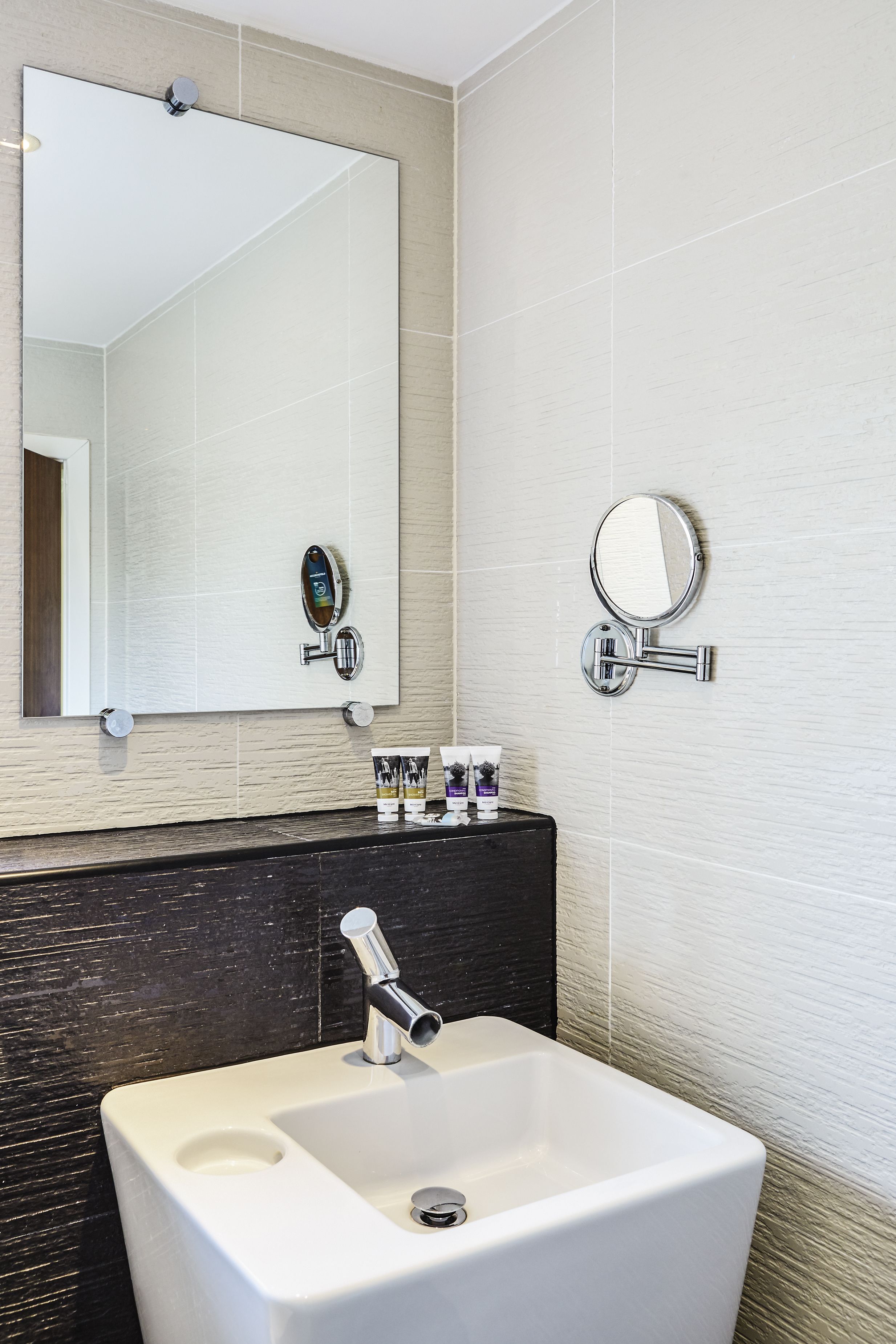 Une salle de bain avec un lavabo blanc, un grand miroir et des articles de toilette posés sur le comptoir.