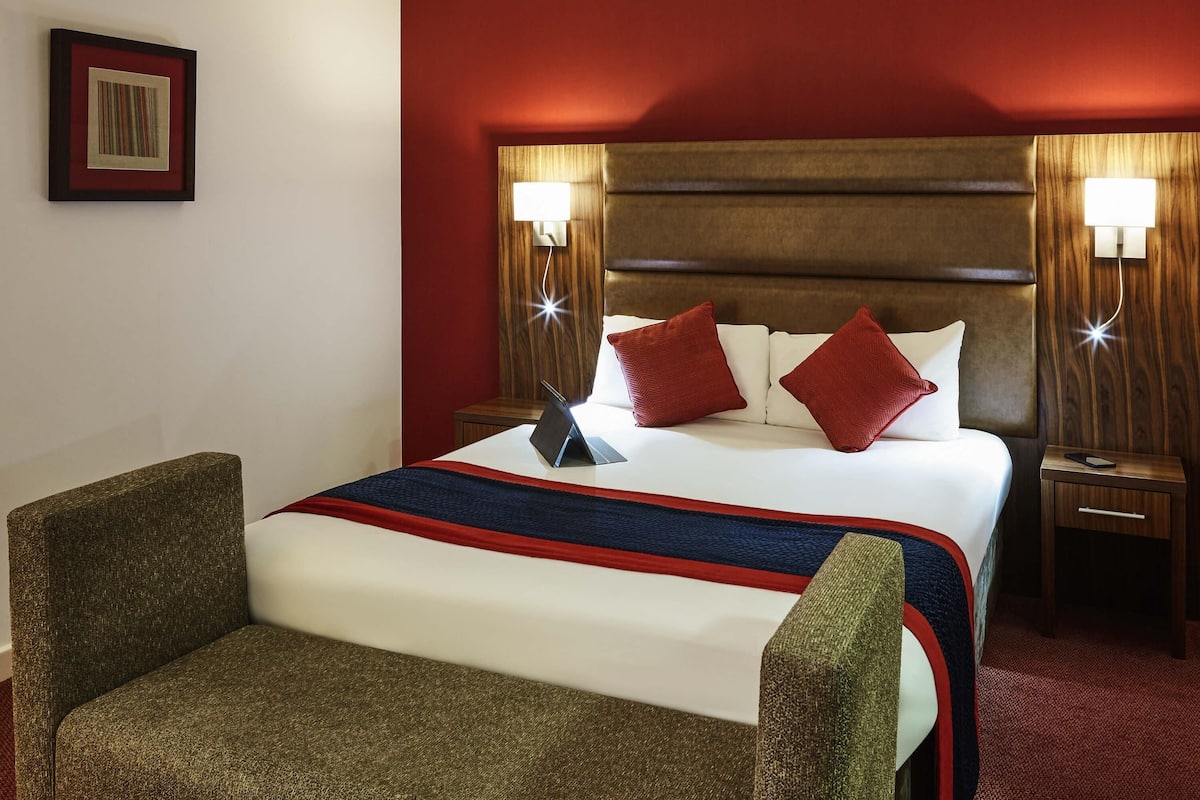 Habitación de hotel con una cama, dos mesitas de noche, un escritorio, una silla y un cuadro en la pared.