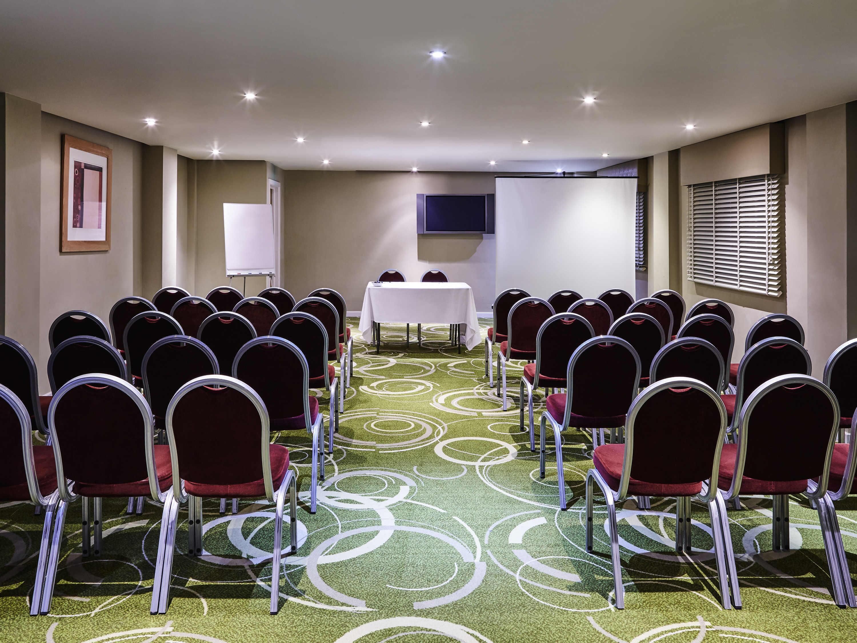 A conference room with rows of chairs, a white table, and a projector screen.