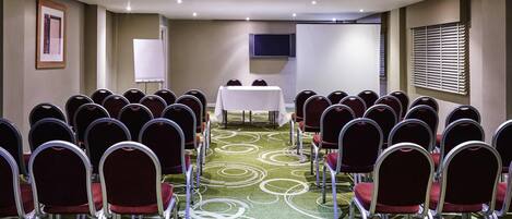A conference room with rows of chairs, a white table, and a projector screen.