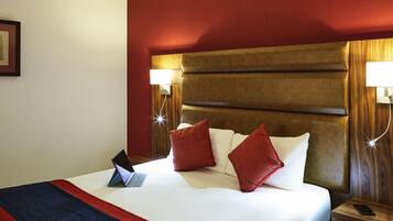 A hotel room with a bed, a bedside table, a lamp, and a laptop on the bed.