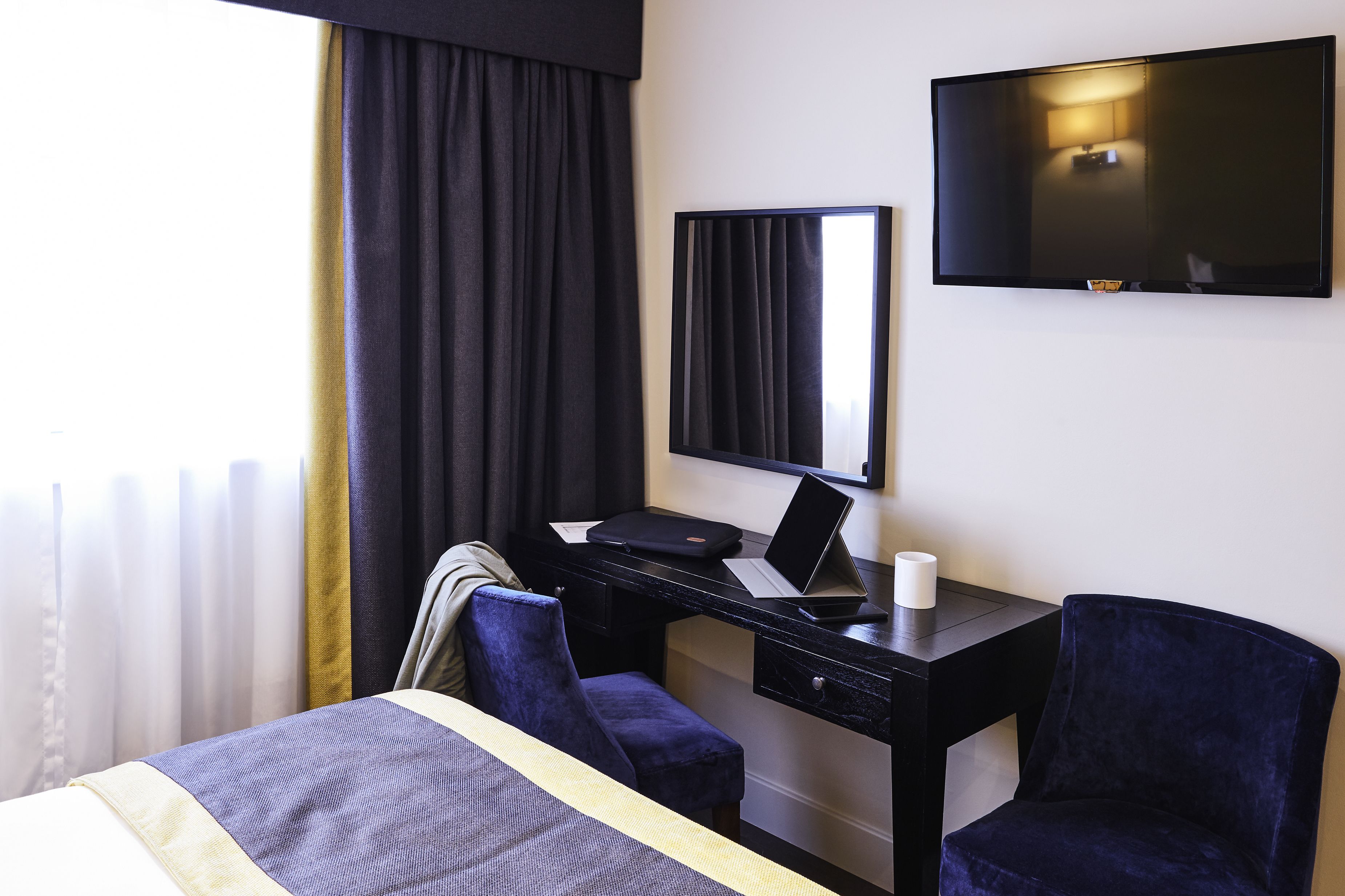 Une chambre d’hôtel équipée d’un lit, d’un bureau avec un ordinateur portable, d’une chaise et d’un téléviseur à écran plat fixé au mur.