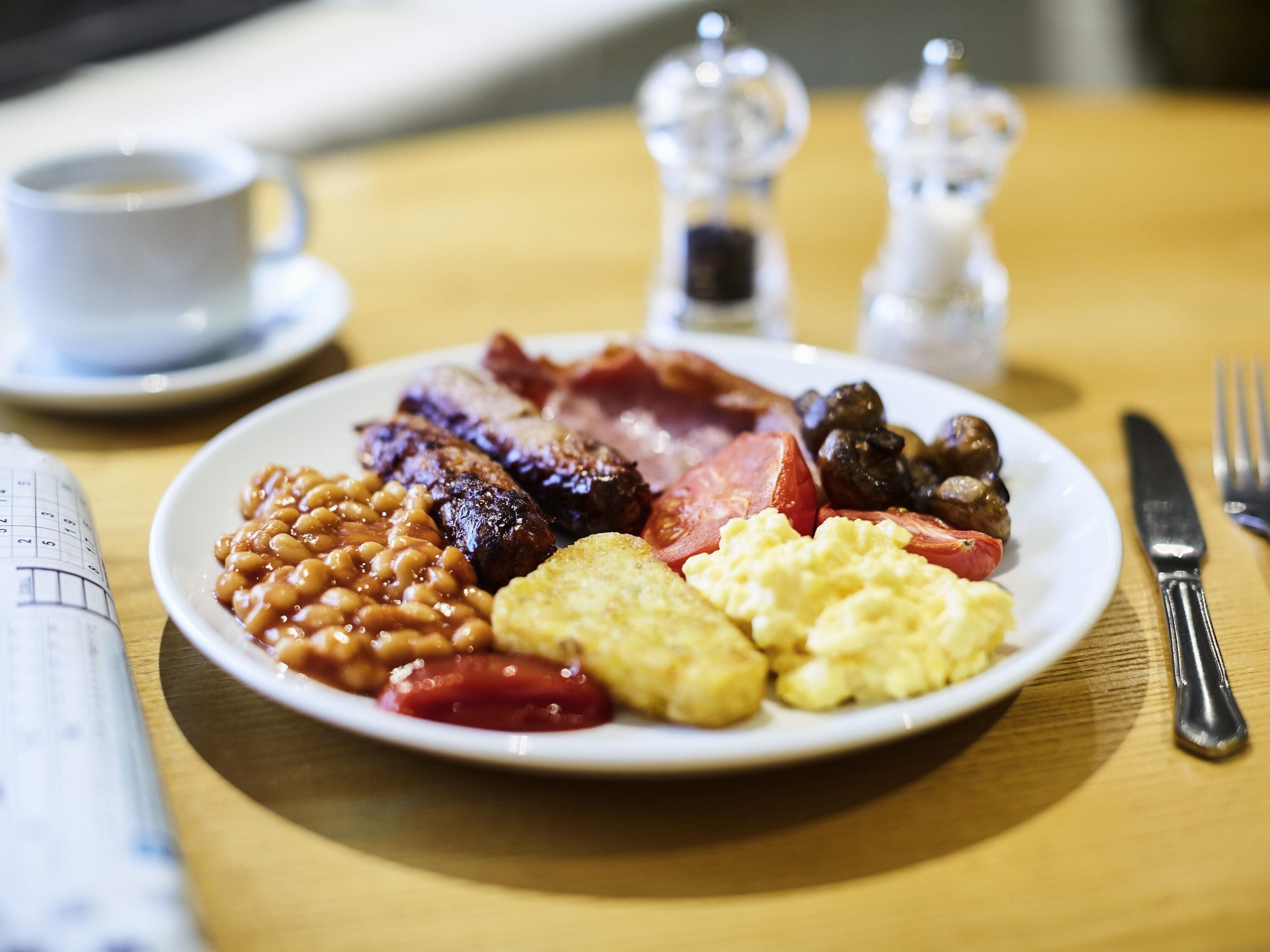 A plate of breakfast food including sausages, beans, eggs, and tomatoes.