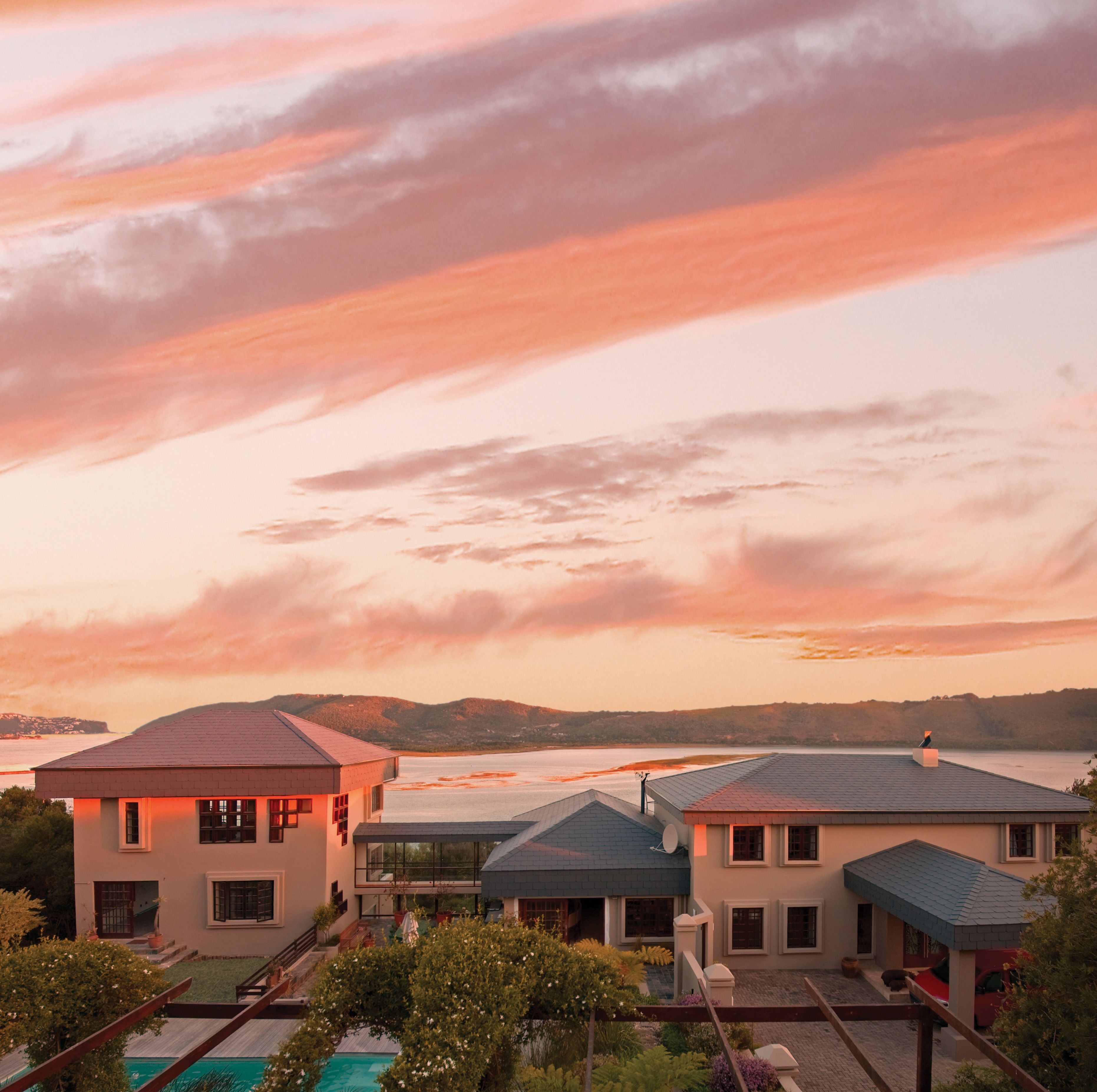 Una zona residencial moderna con varias casas, una piscina y vistas al agua y las colinas al fondo.