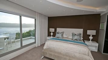 A bedroom with a large window, a bed with a blue accent, and a view of a body of water.