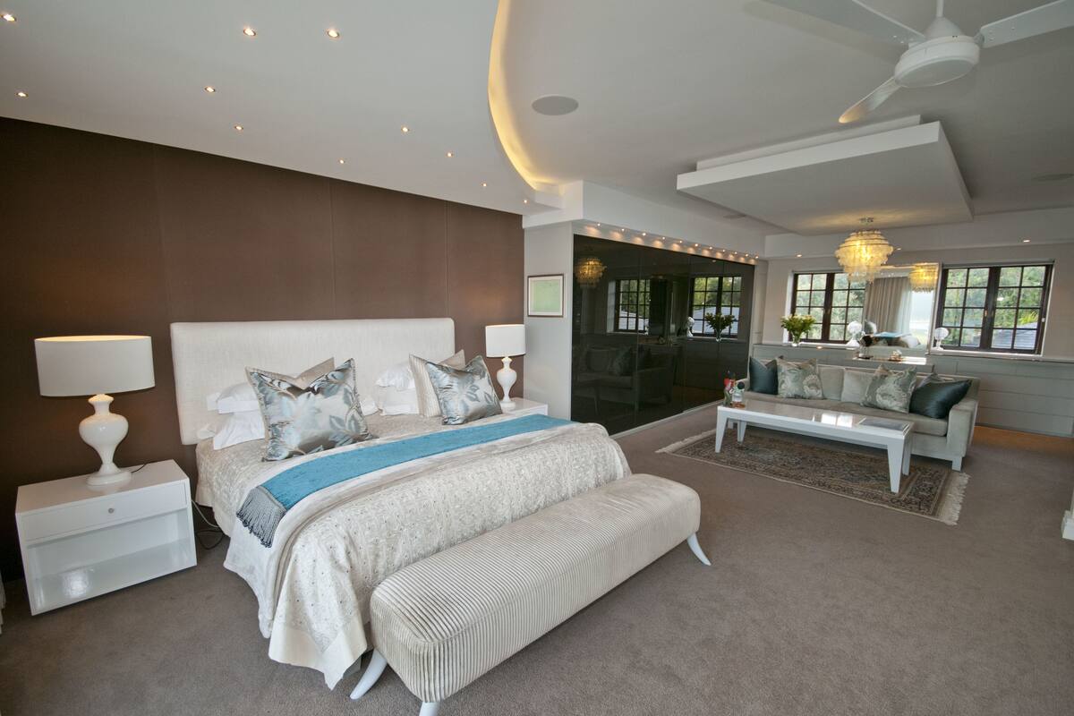 A modern bedroom with a large bed, a nightstand, a bedside table, a sofa, a coffee table, and a chandelier.