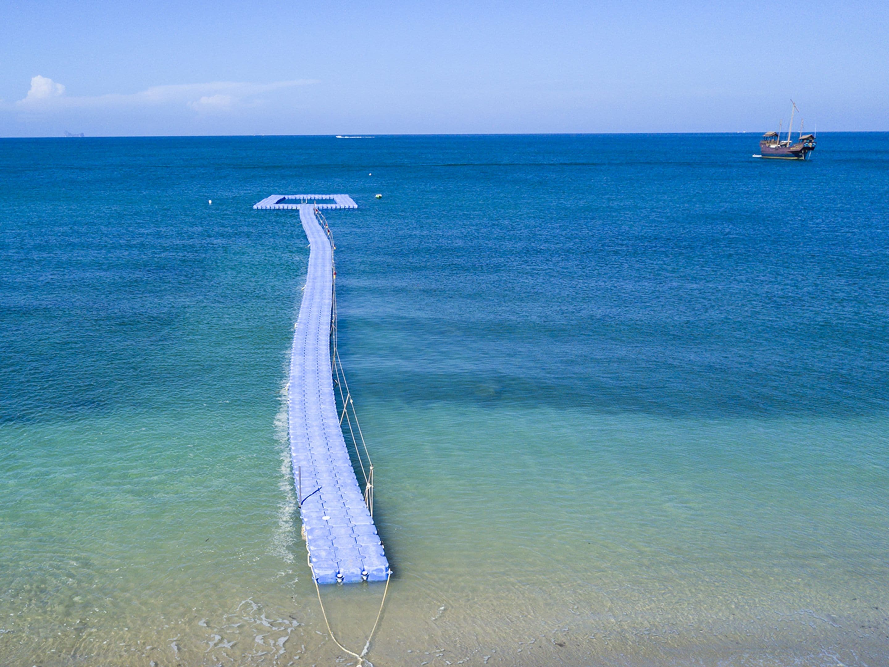 A long, narrow pier extending into the ocean, with a boat anchored at the end.