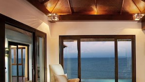 A spacious room with a large window overlooking the sea, a comfortable seating area with a wicker sofa and armchair, and a small table with a vase of flowers and two glasses of wine. - Rawi Warin Resort and Spa (Ko Lanta)